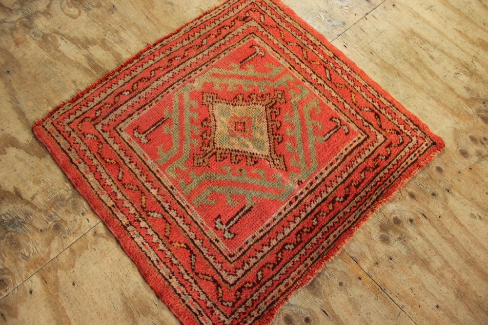 A square hand-knotted antique Oushak wool mat featuring a central geometric diamond medallion in coral red, sage green, and taupe tones. View V