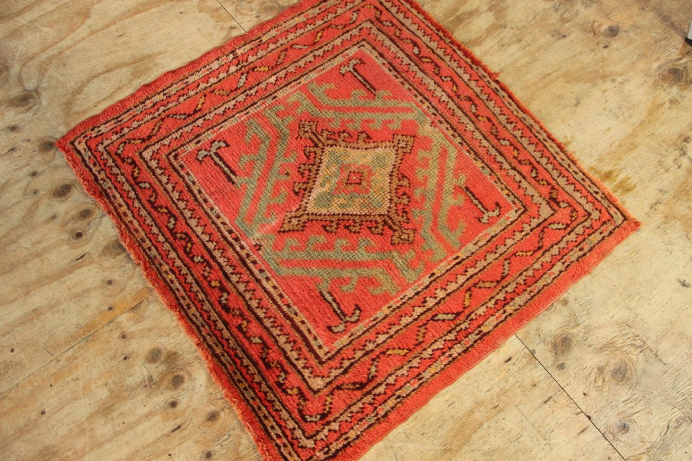 A square hand-knotted antique Oushak wool mat featuring a central geometric diamond medallion in coral red, sage green, and taupe tones. View VI