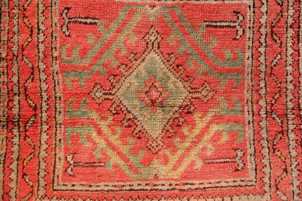 A small square antique hand-knotted wool rug featuring a central diamond medallion surrounded by geometric motifs in terracotta red, sage green, ochre, and dark brown hues. View II