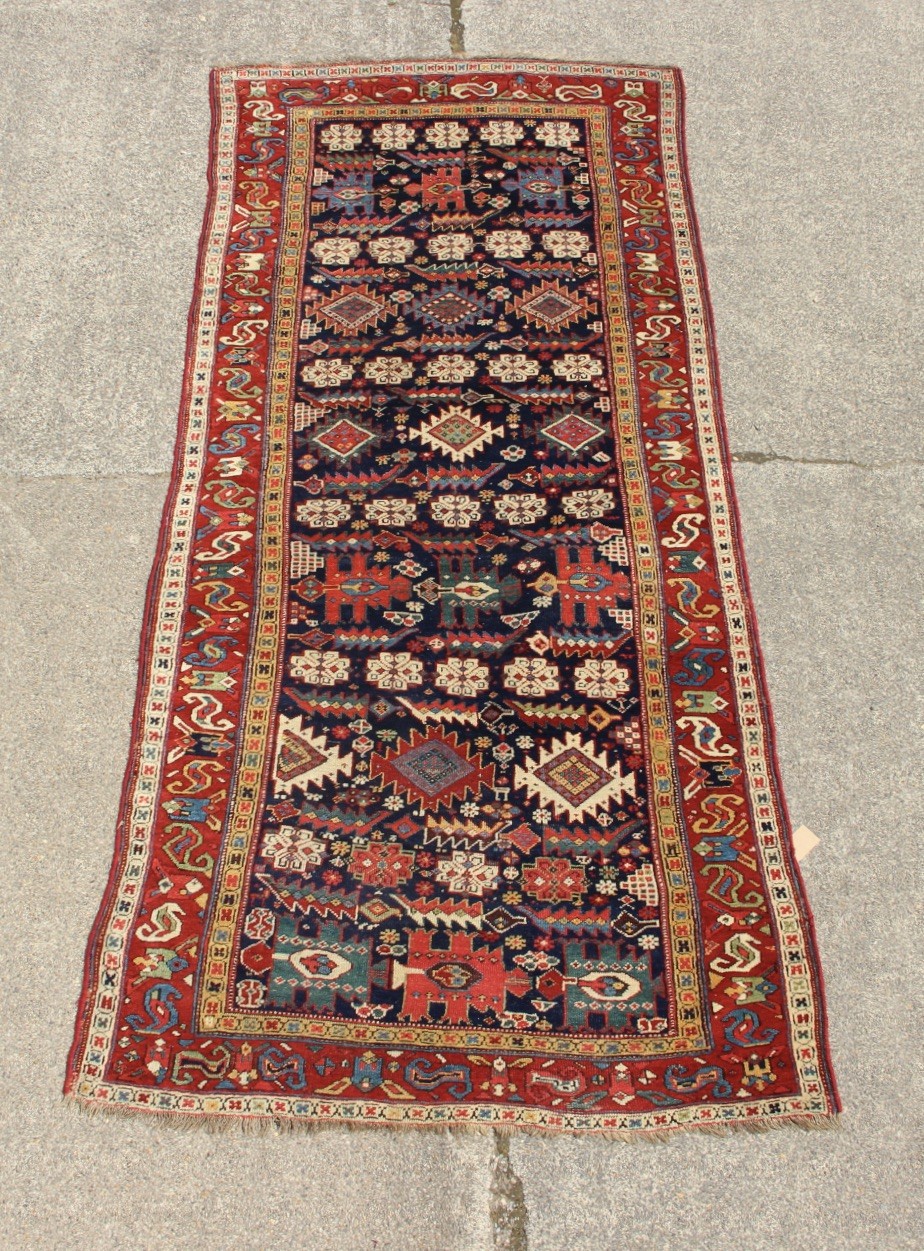 An antique hand-knotted long rug featuring a dark blue central field filled with red, cream, and teal geometric tribal motifs framed by a wide red border.