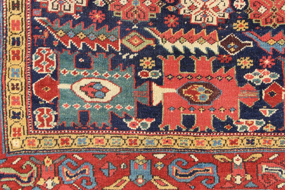 An antique hand-knotted long rug featuring a dark blue central field filled with red, cream, and teal geometric tribal motifs framed by a wide red border. View III