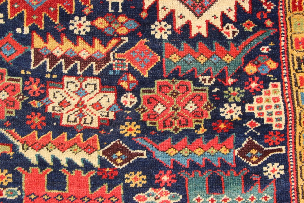 An antique hand-knotted long rug featuring a dark blue central field filled with red, cream, and teal geometric tribal motifs framed by a wide red border. View IV