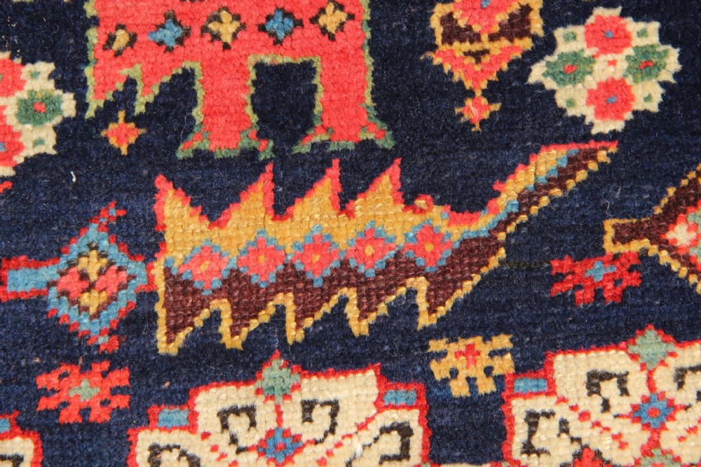 An antique hand-knotted long rug featuring a dark blue central field filled with red, cream, and teal geometric tribal motifs framed by a wide red border. View VI