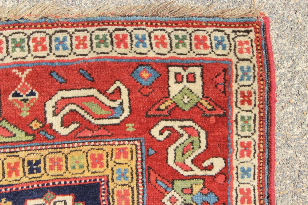 An antique hand-knotted long rug featuring a dark blue central field filled with red, cream, and teal geometric tribal motifs framed by a wide red border. View VII