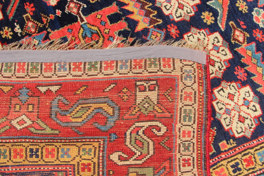 An antique hand-knotted long rug featuring a dark blue central field filled with red, cream, and teal geometric tribal motifs framed by a wide red border. View VIII