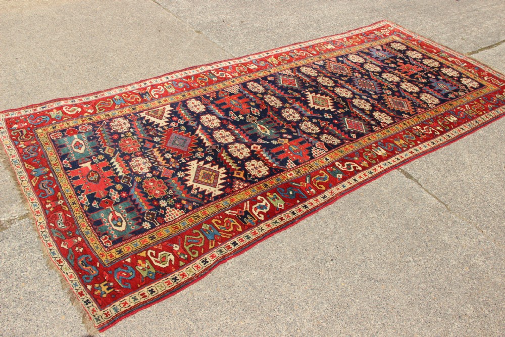 An antique hand-knotted long rug featuring a dark blue central field filled with red, cream, and teal geometric tribal motifs framed by a wide red border. View XI