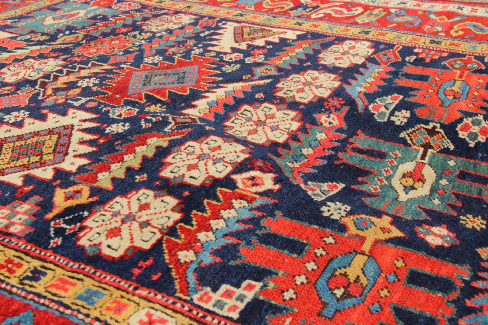 An antique hand-knotted long rug featuring a dark blue central field filled with red, cream, and teal geometric tribal motifs framed by a wide red border. View XII