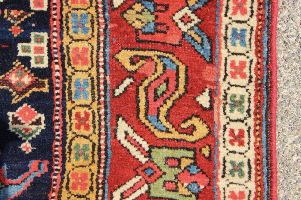 An antique hand-knotted long rug featuring a dark blue central field filled with red, cream, and teal geometric tribal motifs framed by a wide red border. View XIII