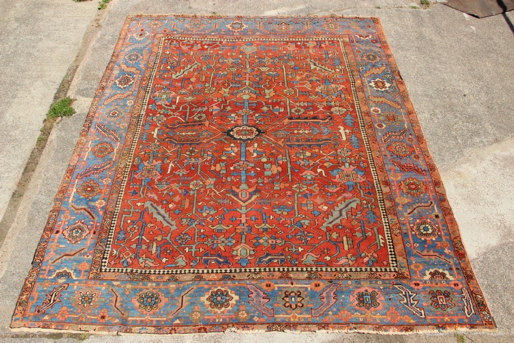 An antique hand-knotted Persian Bakshaish wool carpet featuring a central geometric motif on a terracotta red field framed by a wide blue floral border.