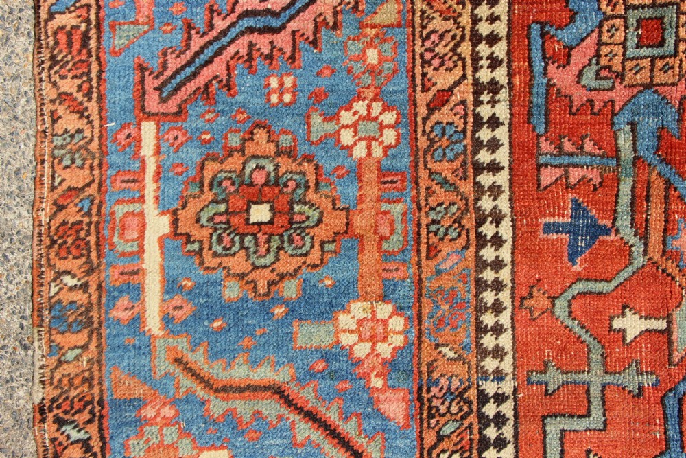 An antique hand-knotted Persian Bakshaish wool carpet featuring a central geometric motif on a terracotta red field framed by a wide blue floral border. View II
