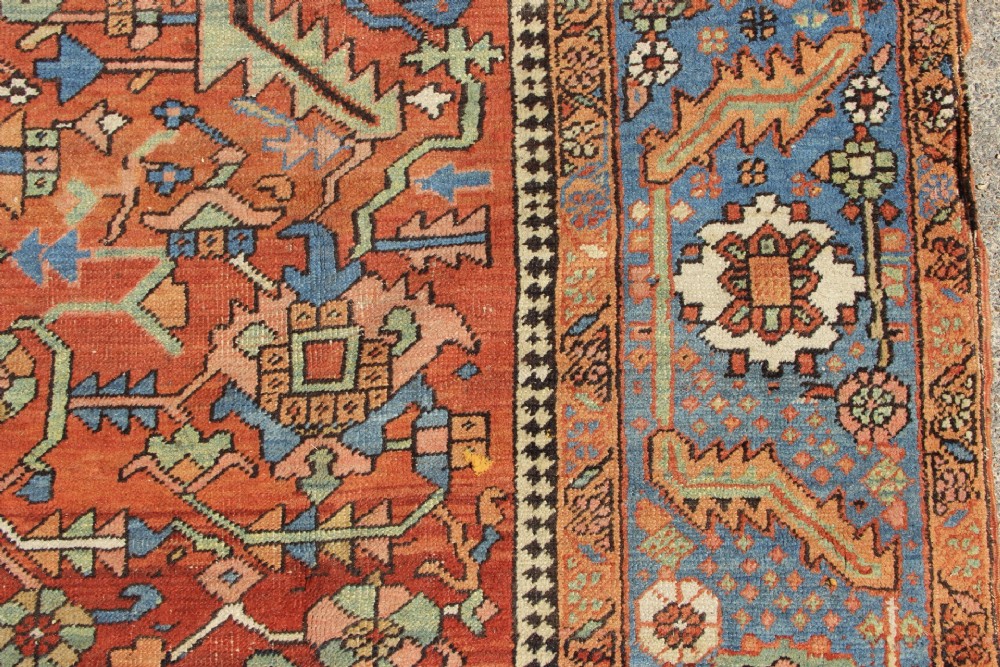 An antique hand-knotted Persian Bakshaish wool carpet featuring a central geometric motif on a terracotta red field framed by a wide blue floral border. View V