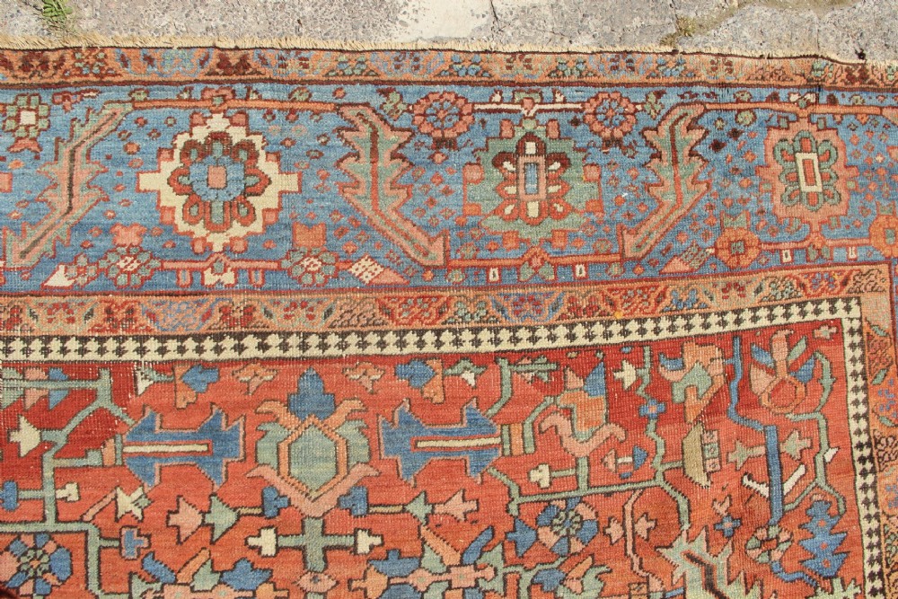 An antique hand-knotted Persian Bakshaish wool carpet featuring a central geometric motif on a terracotta red field framed by a wide blue floral border. View VI