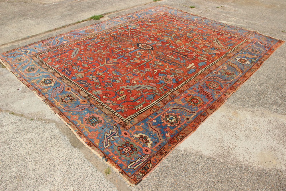 An antique hand-knotted Persian Bakshaish wool carpet featuring a central geometric motif on a terracotta red field framed by a wide blue floral border. View VII