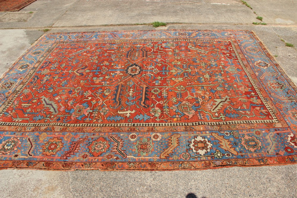 An antique hand-knotted Persian Bakshaish wool carpet featuring a central geometric motif on a terracotta red field framed by a wide blue floral border. View VIII