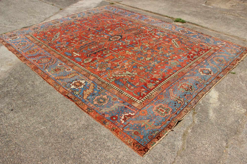 An antique hand-knotted Persian Bakshaish wool carpet featuring a central geometric motif on a terracotta red field framed by a wide blue floral border. View IX