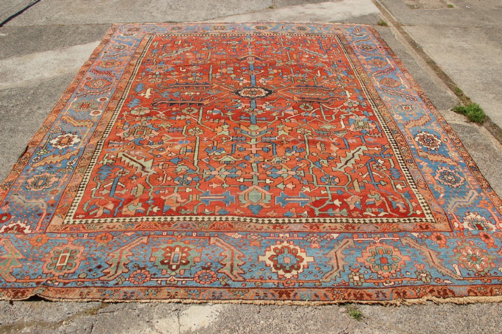 An antique hand-knotted Persian Bakshaish wool carpet featuring a central geometric motif on a terracotta red field framed by a wide blue floral border. View X