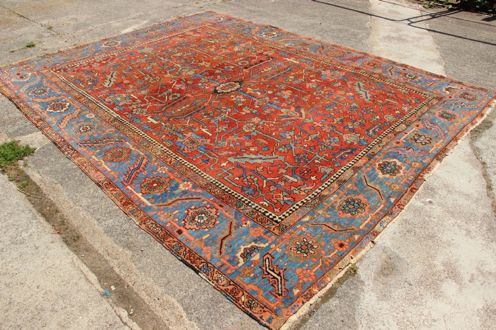 An antique hand-knotted Persian Bakshaish wool carpet featuring a central geometric motif on a terracotta red field framed by a wide blue floral border. View XIII
