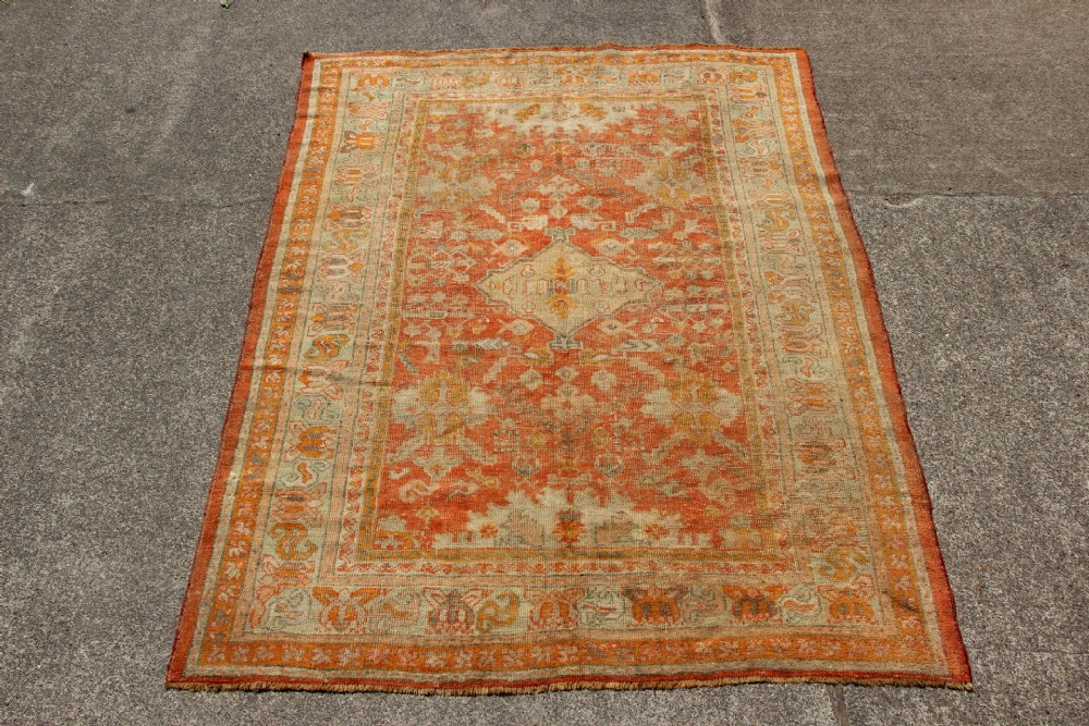 A large hand-woven 19th-century Ghiordes Oushak wool carpet featuring a central diamond medallion, intricate geometric borders, and a terracotta and pale green palette.