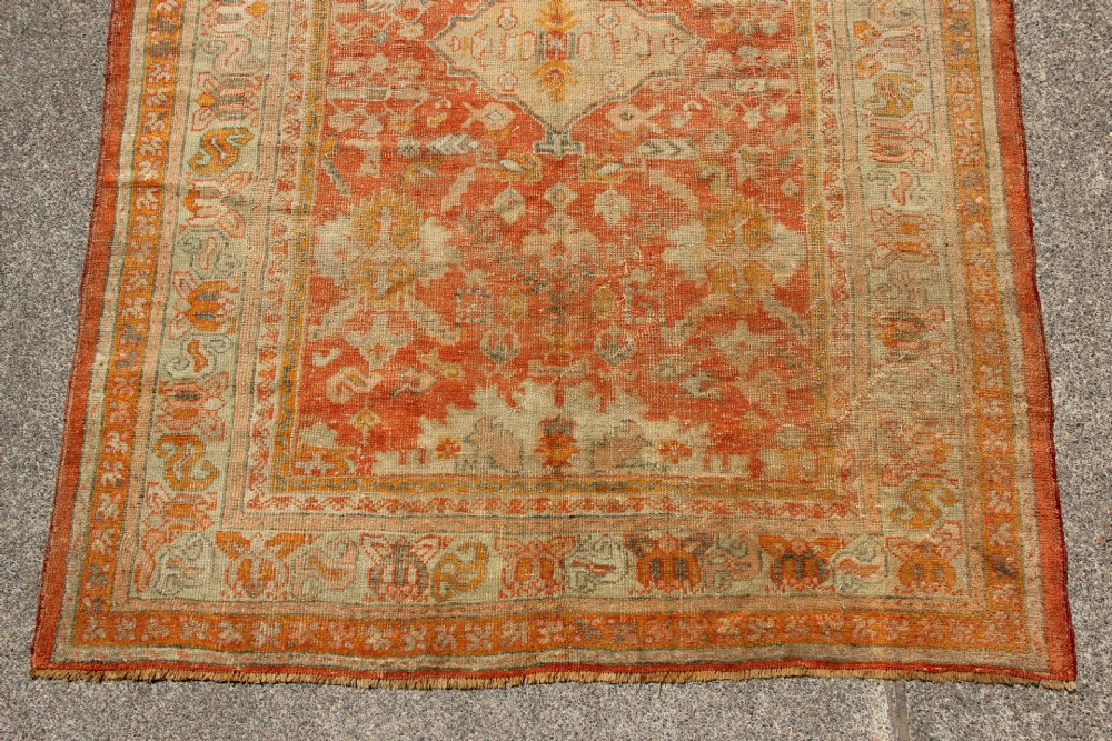 A large hand-woven 19th-century Ghiordes Oushak wool carpet featuring a central diamond medallion, intricate geometric borders, and a terracotta and pale green palette. View II