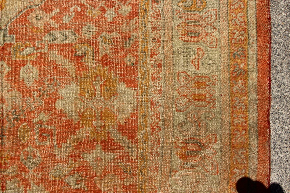A large hand-woven 19th-century Ghiordes Oushak wool carpet featuring a central diamond medallion, intricate geometric borders, and a terracotta and pale green palette. View IV