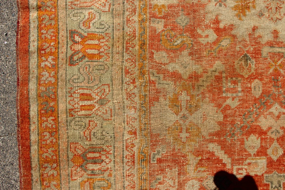 A large hand-woven 19th-century Ghiordes Oushak wool carpet featuring a central diamond medallion, intricate geometric borders, and a terracotta and pale green palette. View VI