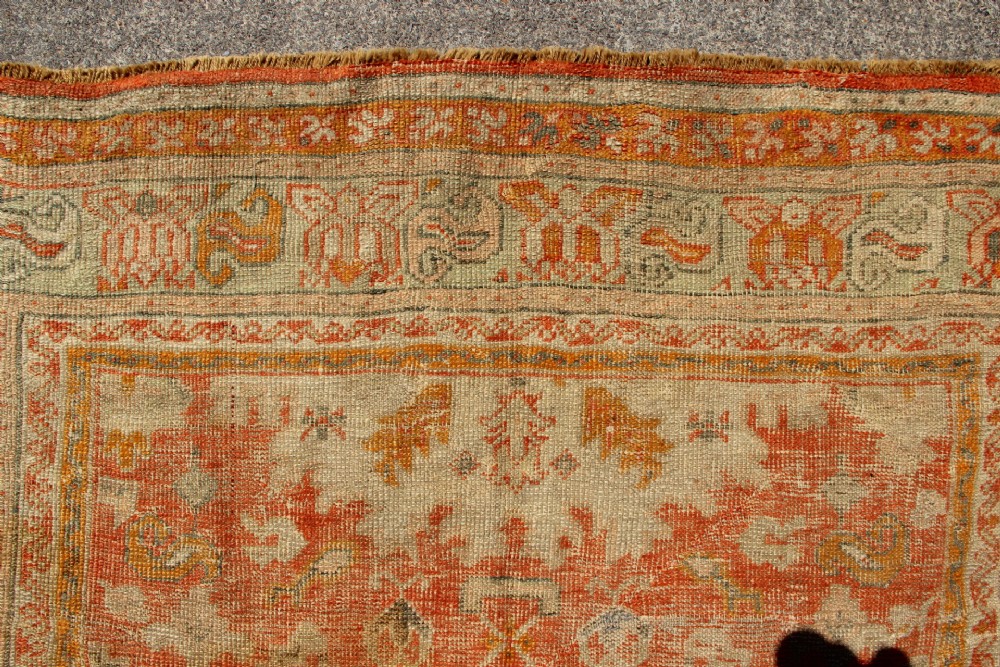 A large hand-woven 19th-century Ghiordes Oushak wool carpet featuring a central diamond medallion, intricate geometric borders, and a terracotta and pale green palette. View VII