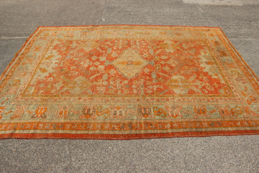 A large hand-woven 19th-century Ghiordes Oushak wool carpet featuring a central diamond medallion, intricate geometric borders, and a terracotta and pale green palette. View IX