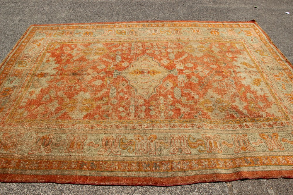 A large hand-woven 19th-century Ghiordes Oushak wool carpet featuring a central diamond medallion, intricate geometric borders, and a terracotta and pale green palette. View XII