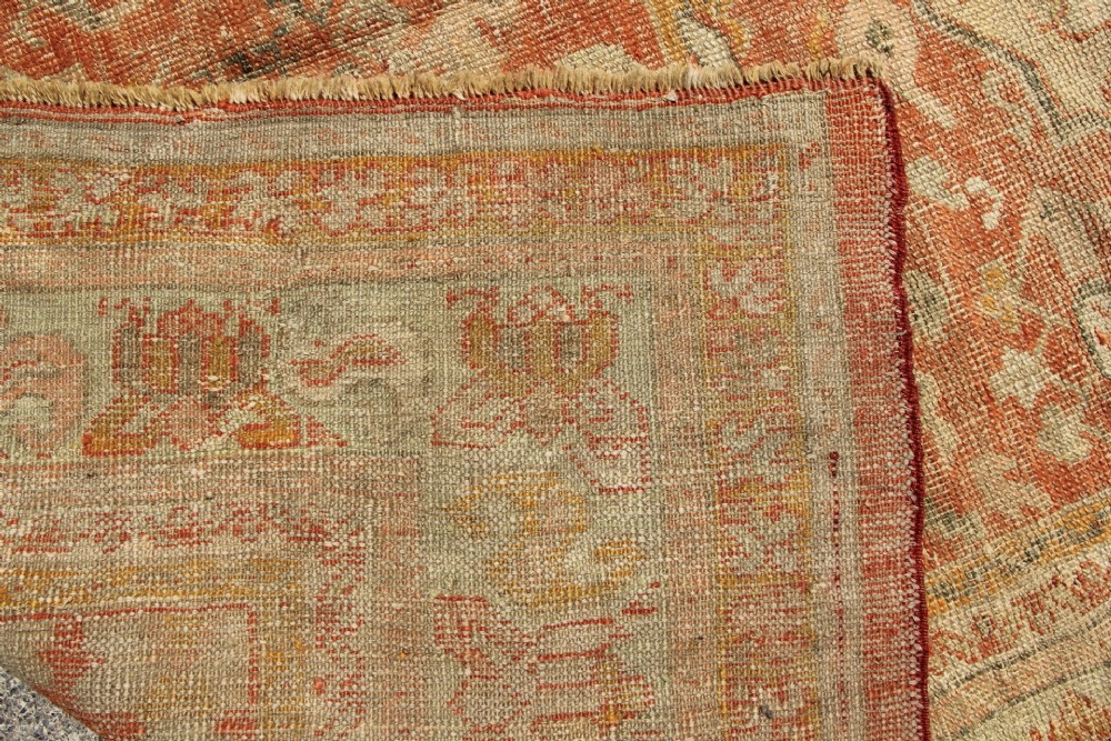 A large hand-woven 19th-century Ghiordes Oushak wool carpet featuring a central diamond medallion, intricate geometric borders, and a terracotta and pale green palette. View XIV