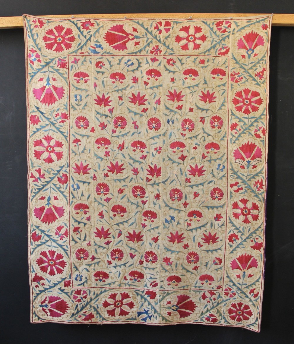A rectangular hand-embroidered suzani textile featuring crimson floral motifs and blue scrolling vines on a cream ground.
