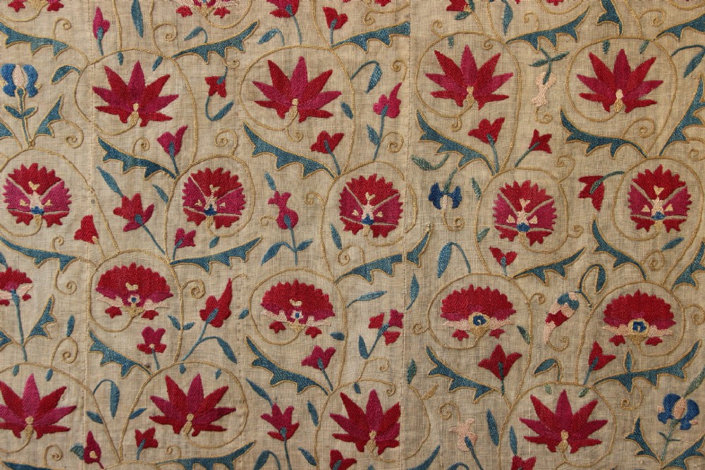 A rectangular hand-embroidered suzani textile featuring crimson floral motifs and blue scrolling vines on a cream ground. View II