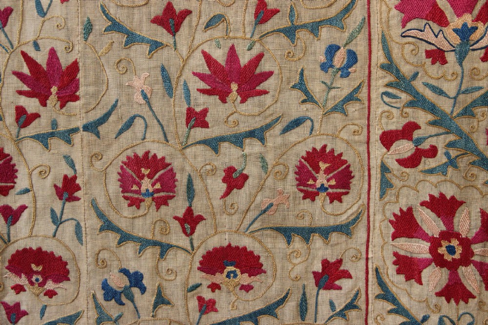 A rectangular hand-embroidered suzani textile featuring crimson floral motifs and blue scrolling vines on a cream ground. View IV