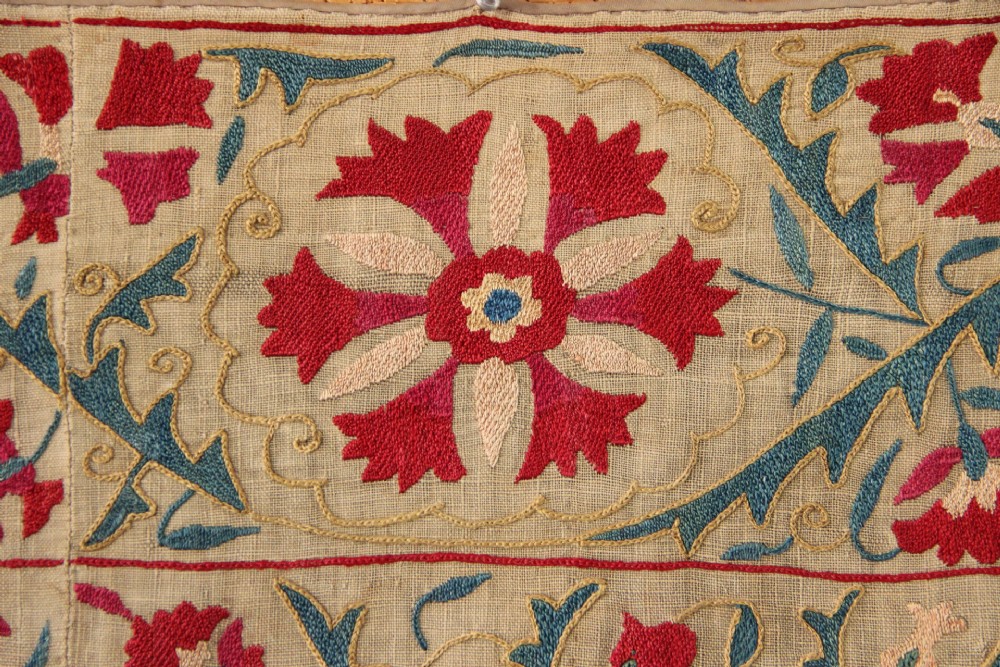 A rectangular hand-embroidered suzani textile featuring crimson floral motifs and blue scrolling vines on a cream ground. View VI