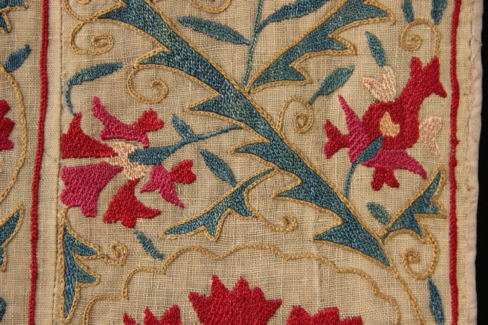 A rectangular hand-embroidered suzani textile featuring crimson floral motifs and blue scrolling vines on a cream ground. View VII