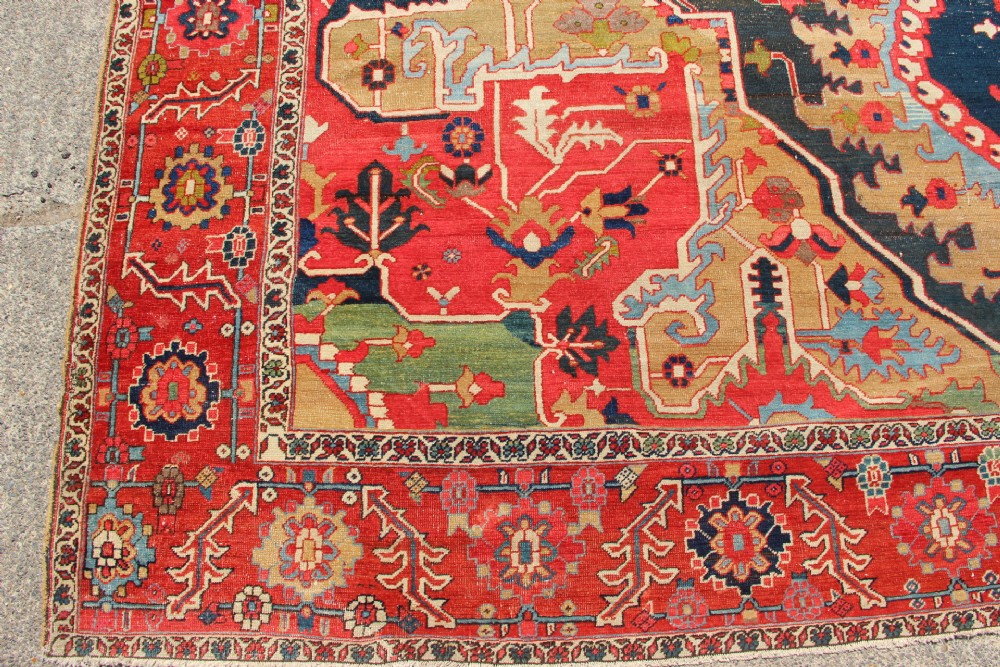 A large hand-knotted Persian Serapi carpet featuring a central geometric medallion in ochre and navy blue, surrounded by a navy field and wide terracotta red border. View II