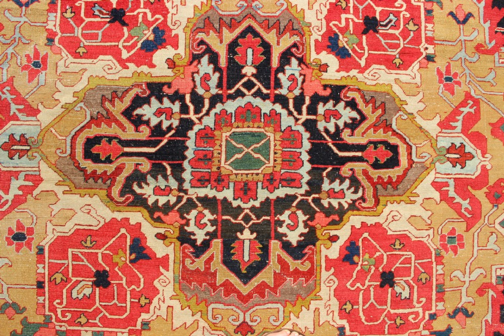 A large hand-knotted Persian Serapi carpet featuring a central geometric medallion in ochre and navy blue, surrounded by a navy field and wide terracotta red border. View VI