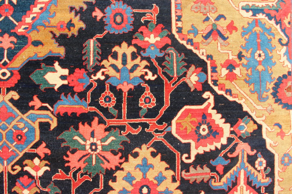 A large hand-knotted Persian Serapi carpet featuring a central geometric medallion in ochre and navy blue, surrounded by a navy field and wide terracotta red border. View VIII