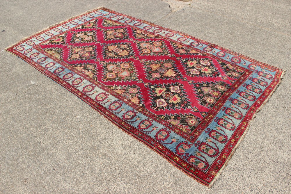 An antique Caucasian Karabagh carpet with a crimson red field displaying stepped geometric medallions framed by a sky blue border. View II