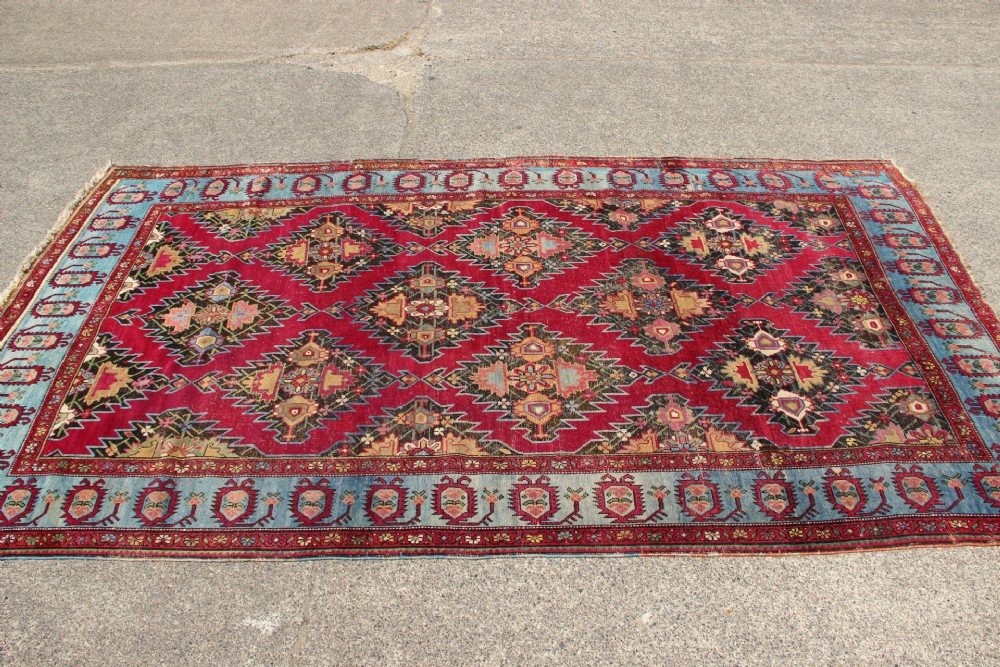 An antique Caucasian Karabagh carpet with a crimson red field displaying stepped geometric medallions framed by a sky blue border. View III