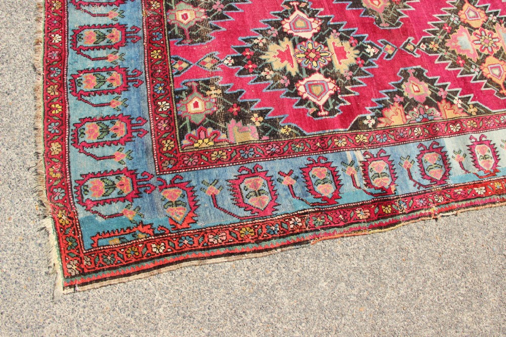 An antique Caucasian Karabagh carpet with a crimson red field displaying stepped geometric medallions framed by a sky blue border. View VII