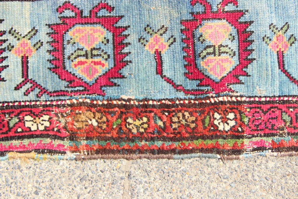 An antique Caucasian Karabagh carpet with a crimson red field displaying stepped geometric medallions framed by a sky blue border. View VIII
