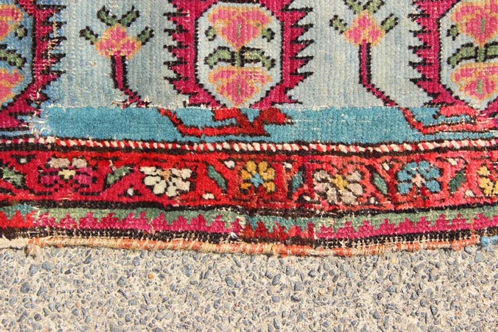 An antique Caucasian Karabagh carpet with a crimson red field displaying stepped geometric medallions framed by a sky blue border. View IX