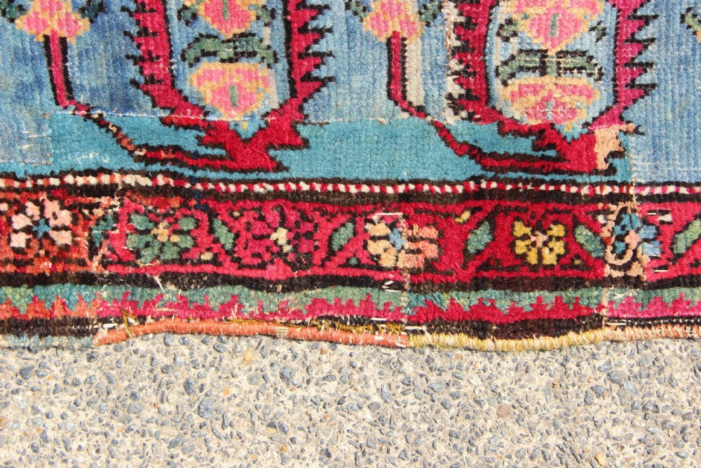 An antique Caucasian Karabagh carpet with a crimson red field displaying stepped geometric medallions framed by a sky blue border. View X