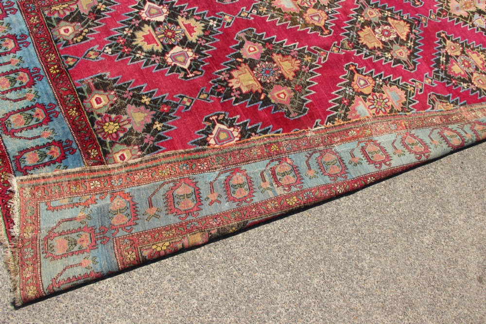 An antique Caucasian Karabagh carpet with a crimson red field displaying stepped geometric medallions framed by a sky blue border. View XI