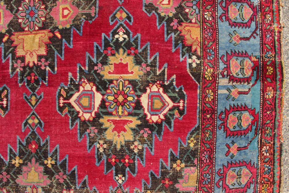 An antique Caucasian Karabagh carpet with a crimson red field displaying stepped geometric medallions framed by a sky blue border. View XII