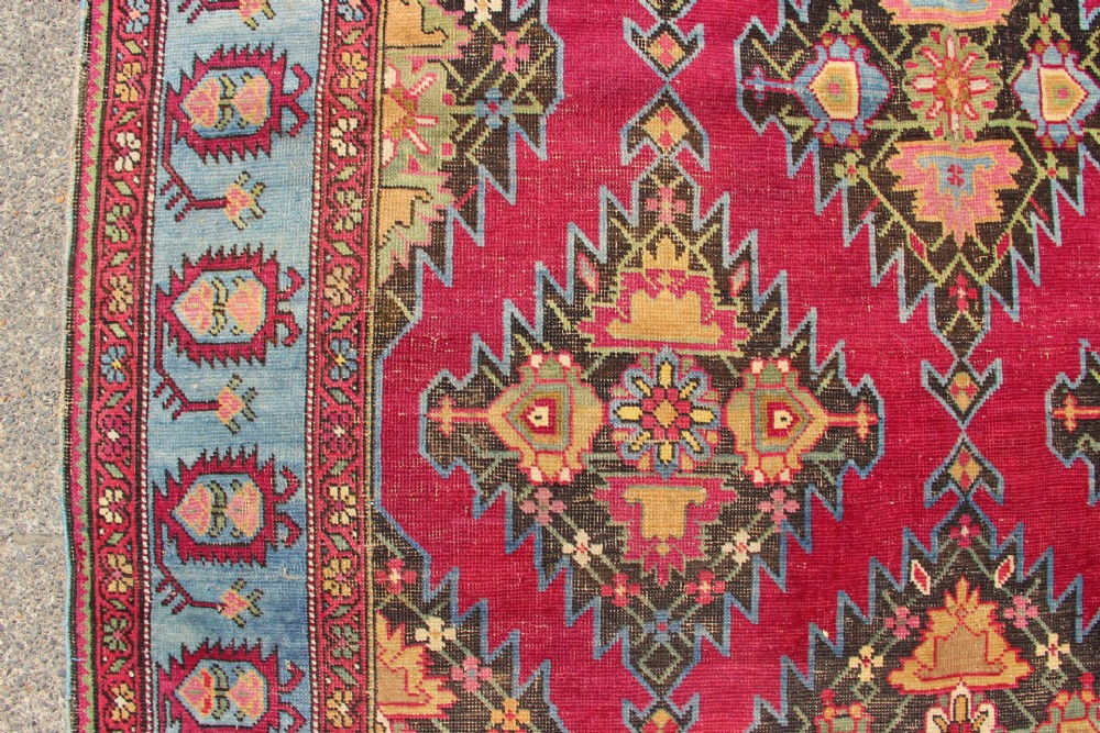 An antique Caucasian Karabagh carpet with a crimson red field displaying stepped geometric medallions framed by a sky blue border. View XIV