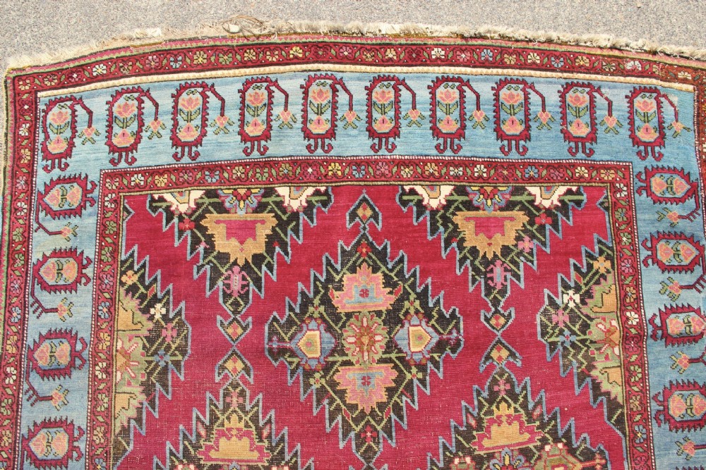 An antique Caucasian Karabagh carpet with a crimson red field displaying stepped geometric medallions framed by a sky blue border. View XV