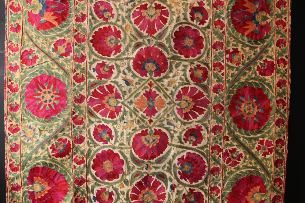 A rectangular hand-embroidered antique Suzani textile featuring red and pink floral medallions on a cream background with green vine borders. View II