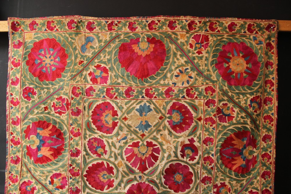 A rectangular hand-embroidered antique Suzani textile featuring red and pink floral medallions on a cream background with green vine borders. View III