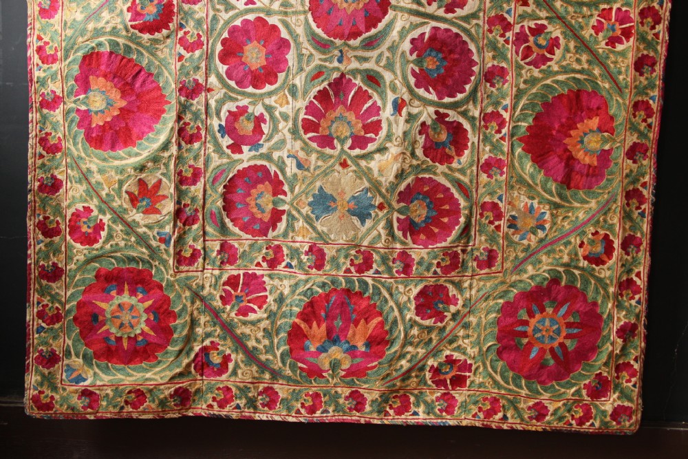 A rectangular hand-embroidered antique Suzani textile featuring red and pink floral medallions on a cream background with green vine borders. View IV
